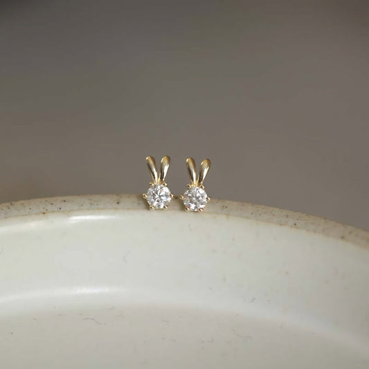 A pair of 9ct solid gold bunny ears studs, reflecting the light to emphasize their handmade charm and playful design.
